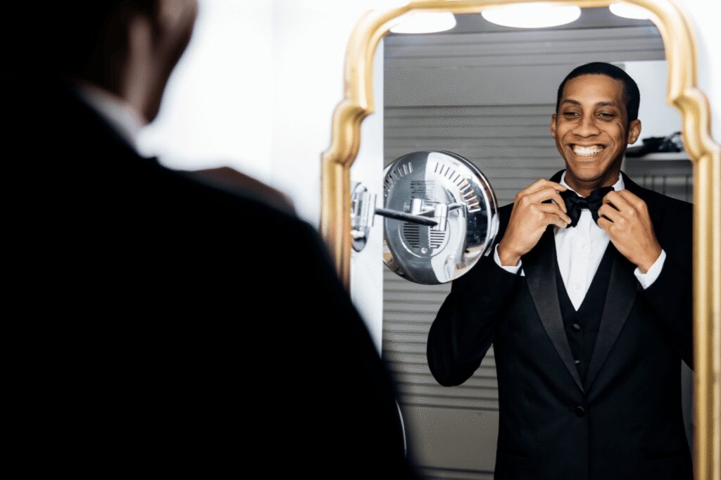 Groom adjusting his tie in hotel room mirror preparing for wedding day